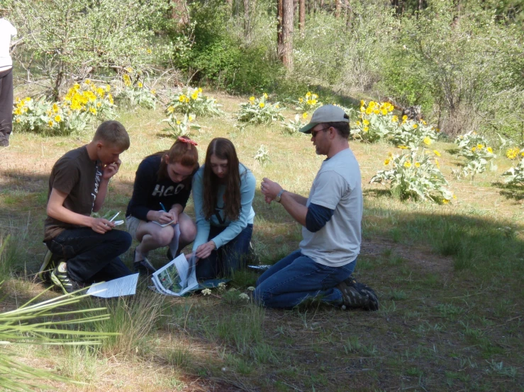 several people sitting and standing near some flowers