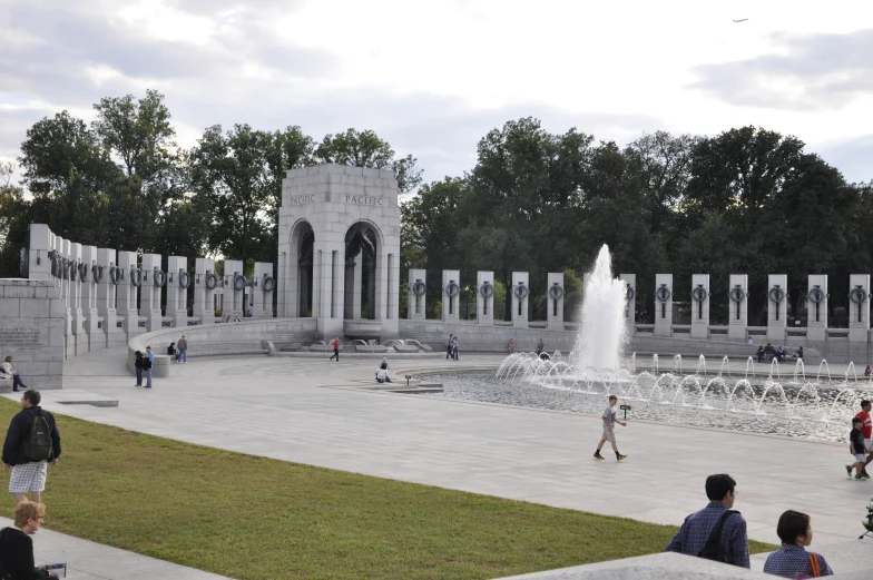 people walking and standing around in front of a water fountain