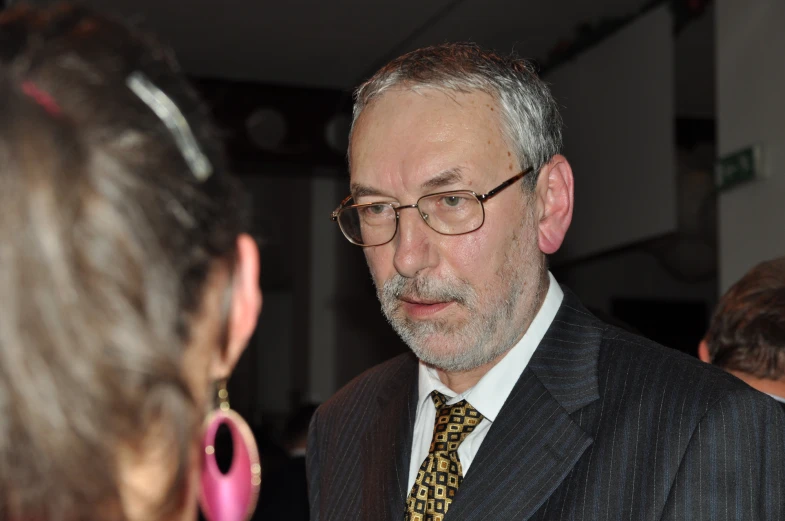 a man wearing glasses talking with another person in front