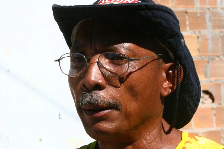 man with glasses and hat in front of brick wall