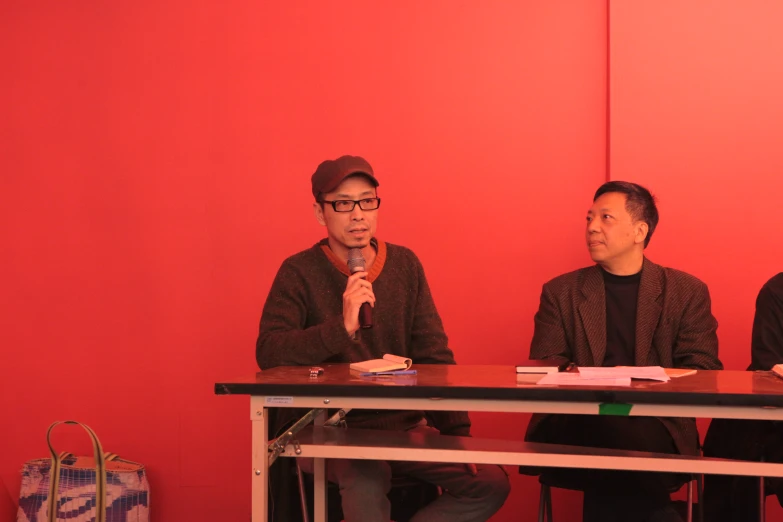 two men are sitting at a table while one man is speaking into a microphone