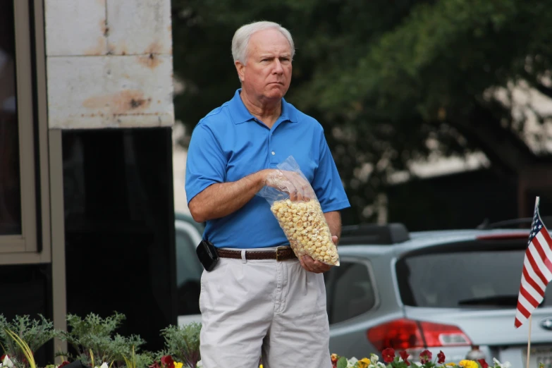 a man is standing near a building holding a bag of popcorn