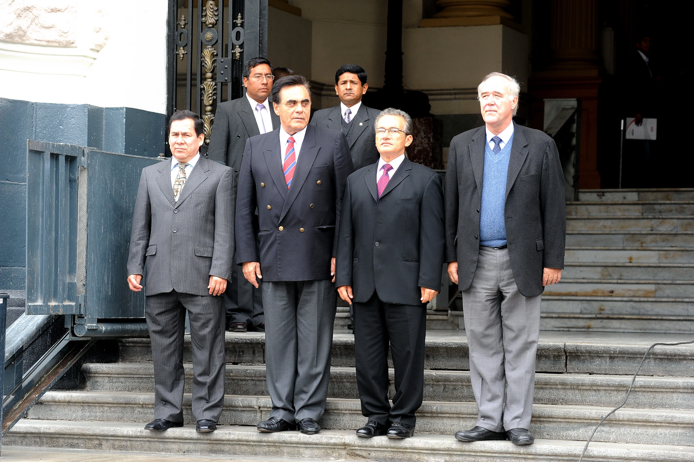 seven people in suits stand on the steps of the building