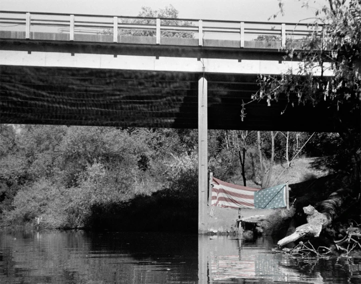 an american flag is hanging in the river next to a bridge