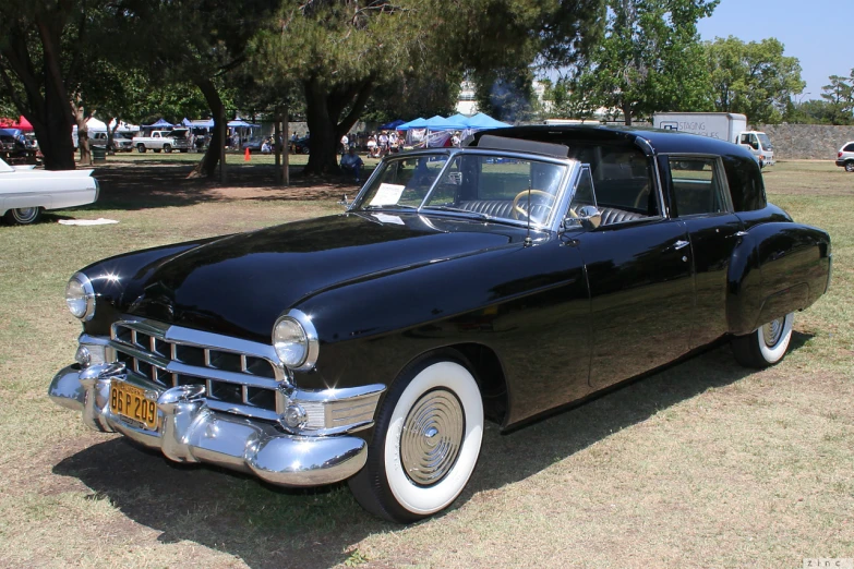 a classic car parked in a field next to a bunch of trees