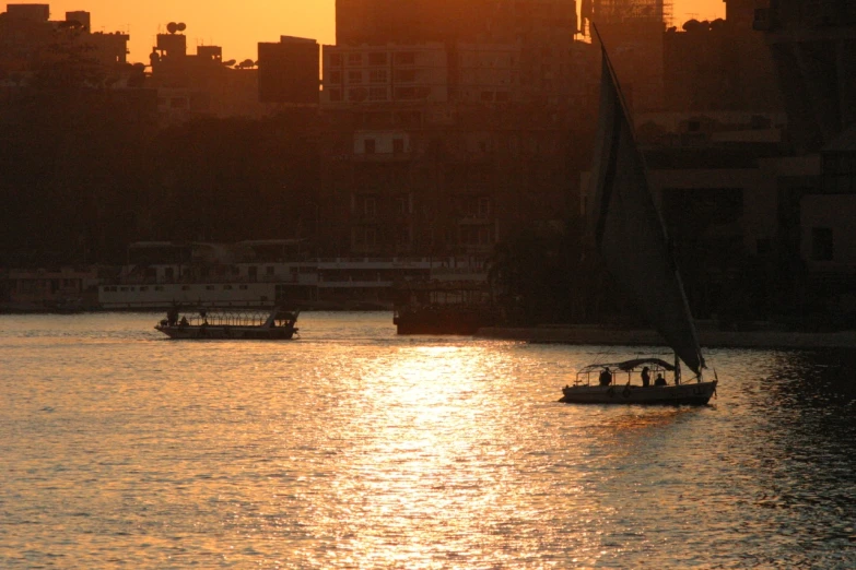 two sail boats sailing in the water with buildings in the background