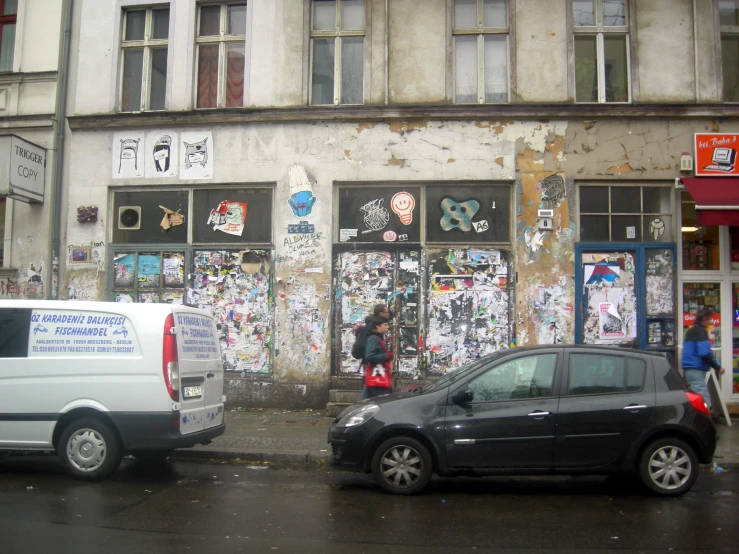 a city street with graffiti covered store fronts, parked cars and people