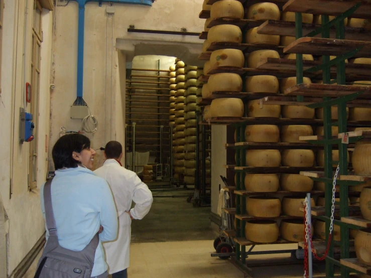 two people standing in a warehouse looking at a bunch of cheese