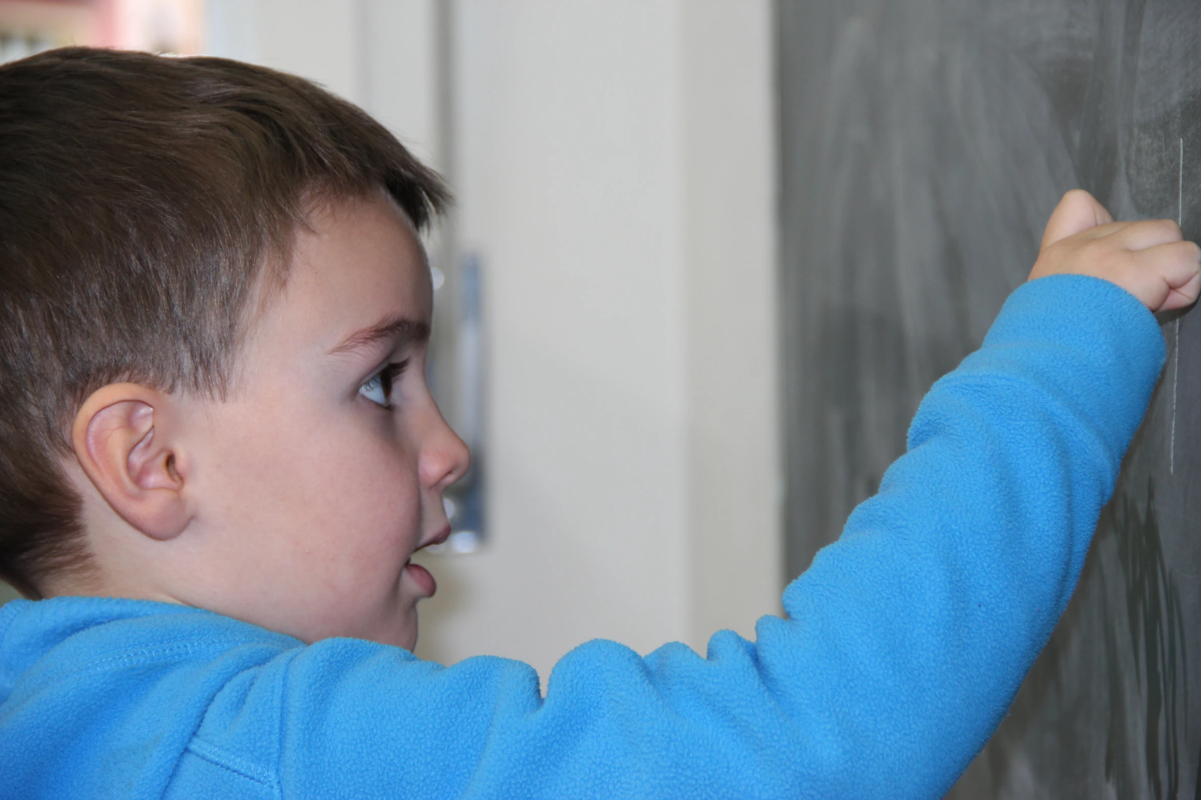 the boy in the blue jacket is writing on a black board