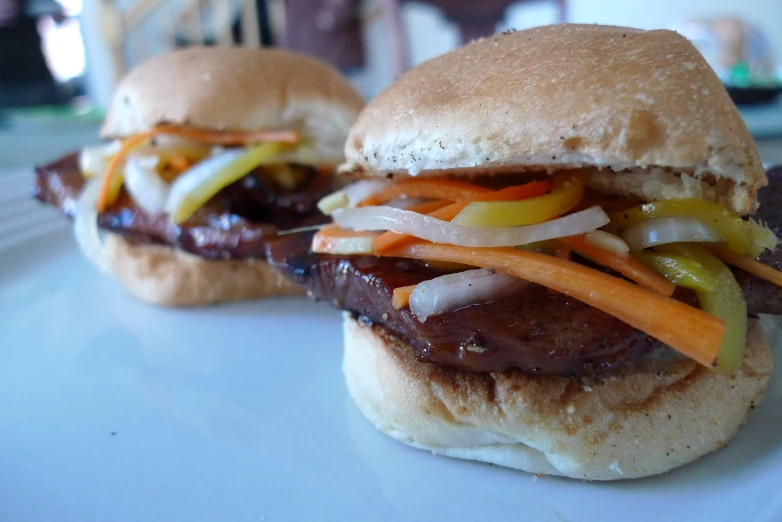 two beef sandwiches with carrots, onions and peppers