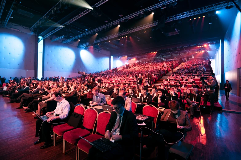 there are many people sitting in a room and there is a speaker on the stage