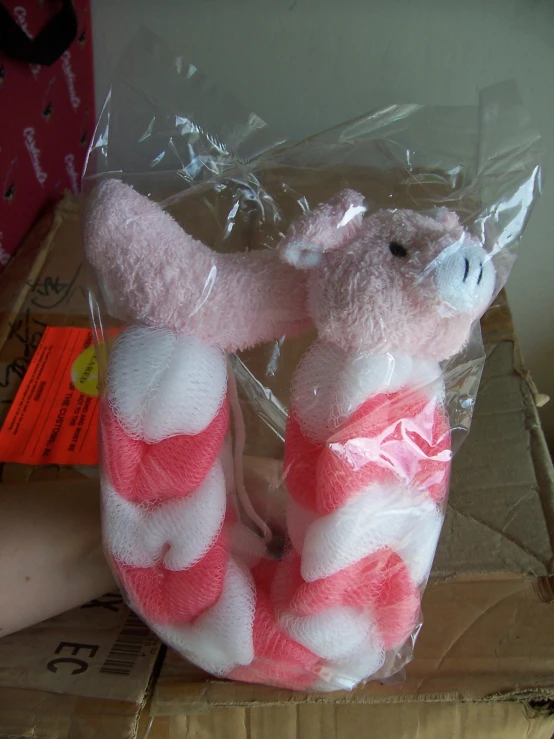 a pink and white teddy bear with striped legs wrapped in plastic