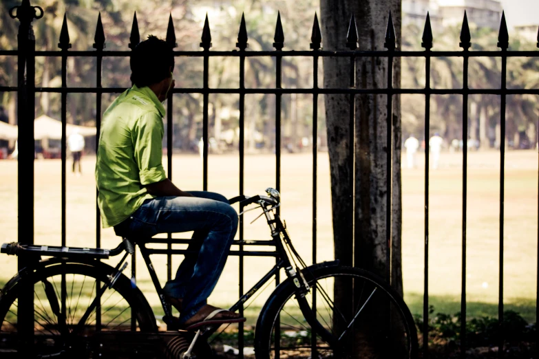 a man sitting on a bicycle next to a metal fence