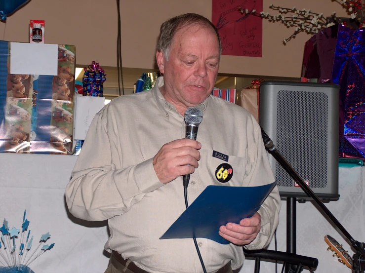 a man holding a microphone, standing with papers and a piece of paper