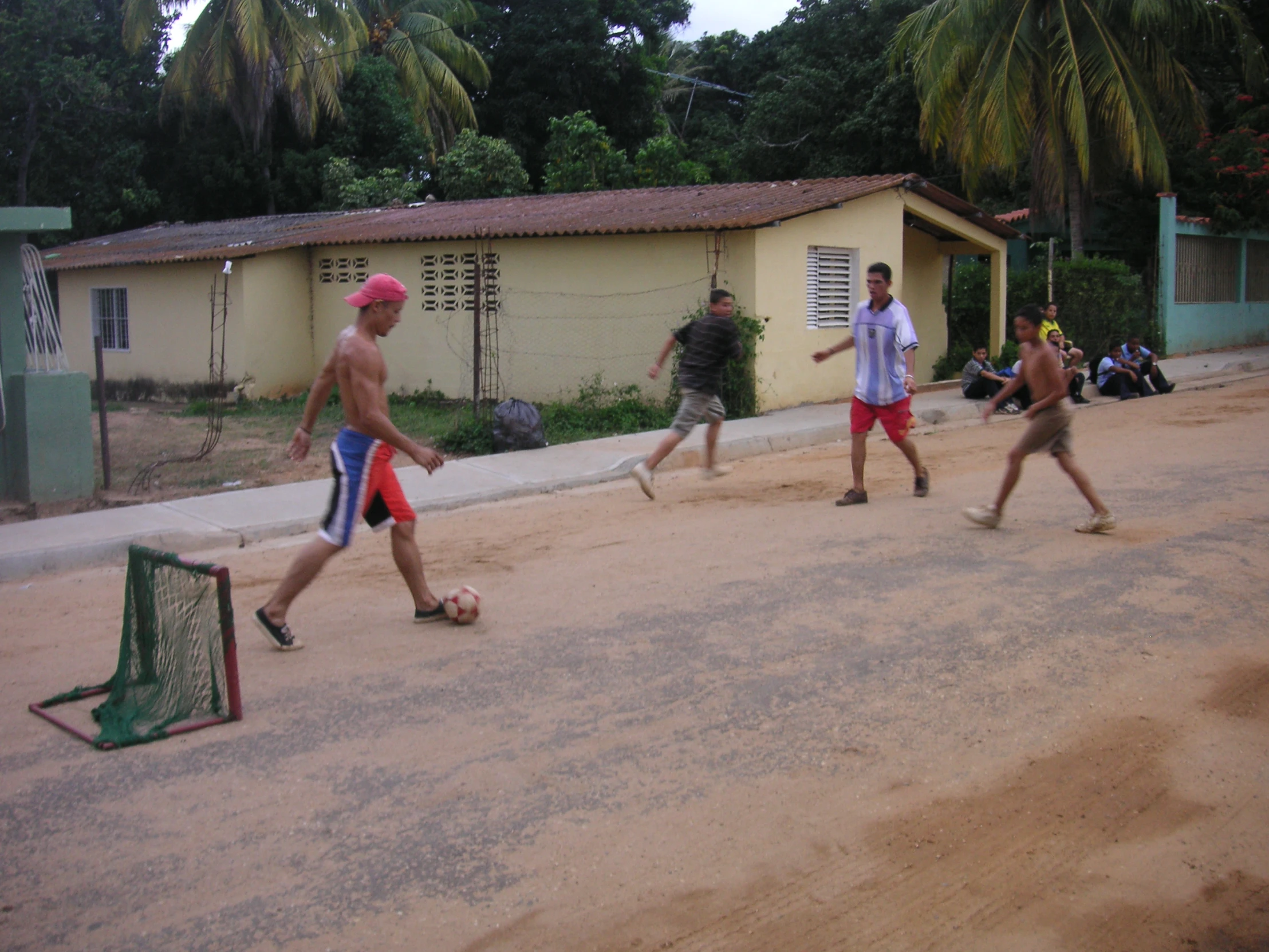 four boys playing ball on a sandy street