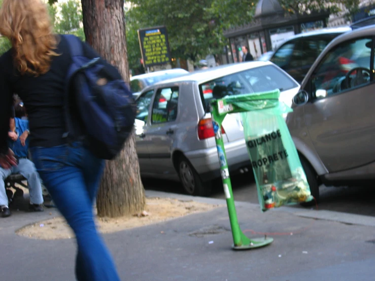 a person wearing blue jeans walking past a green traffic sign