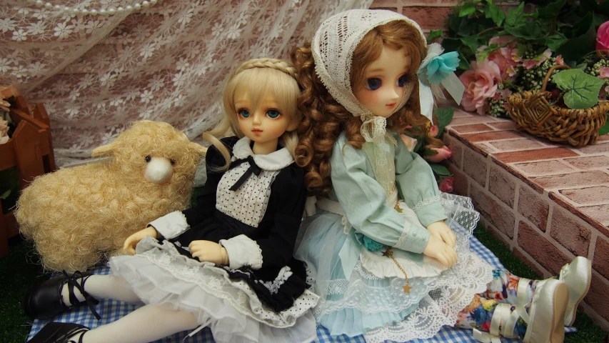 two dolls sitting side by side on a bed next to teddy bear