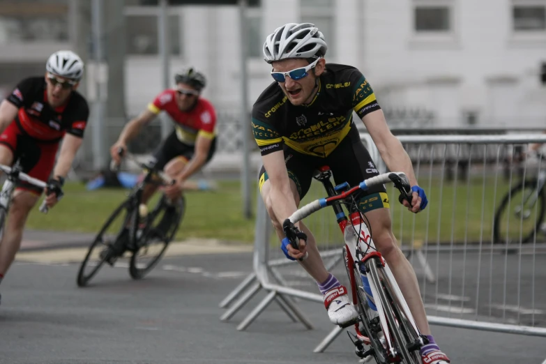 three men riding bikes on a road with buildings in the background