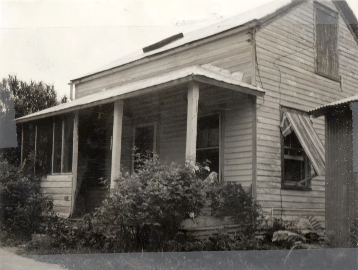 an old picture of a small house with flowers growing around the windows