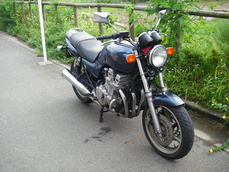 a black motorcycle parked near some plants on the side of a road