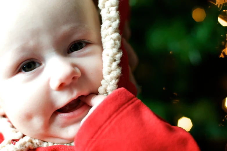 a baby wearing a red sweater and a santa clause cap with christmas lights in the background