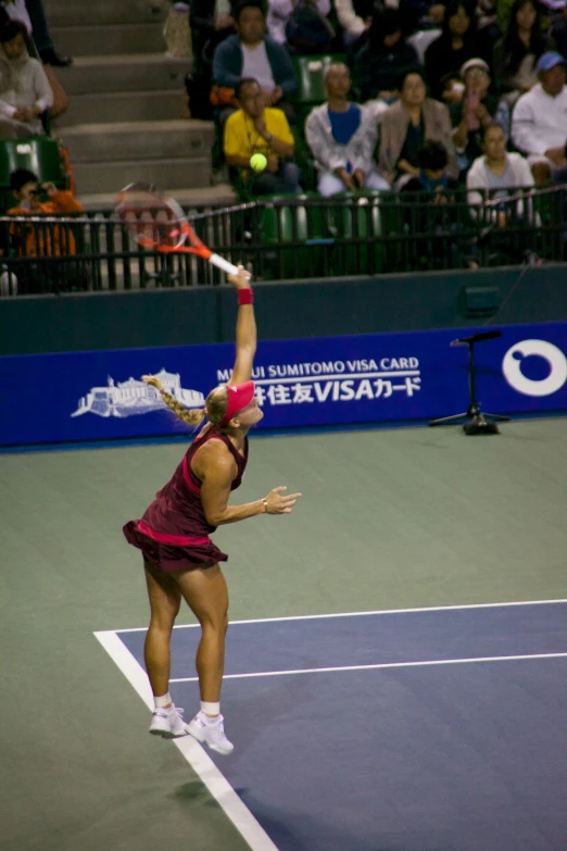 woman in maroon outfit hitting tennis ball on court