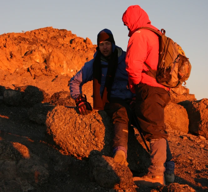 two people hiking up a hill with a backpack on their shoulders