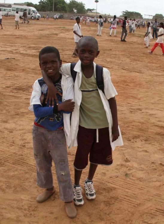 a boy and girl standing on sand with other people in background