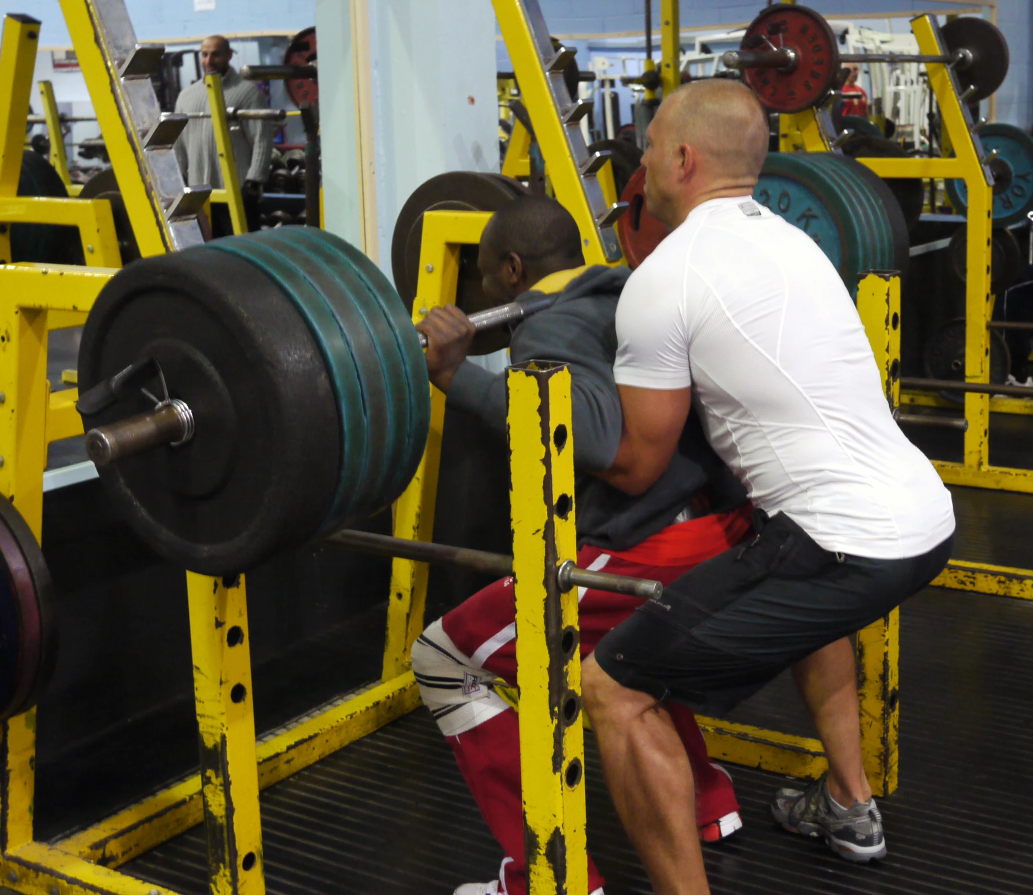 a man lifts up his weight as another squats on the bar in a gym