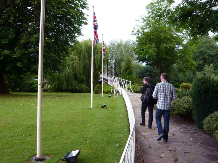 two people walk along a pathway near an american flag pole