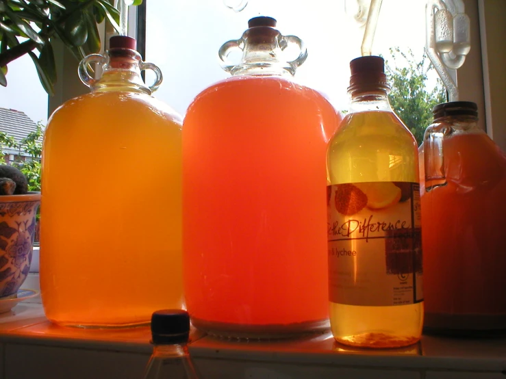 three jars filled with bright liquid sit on a window sill