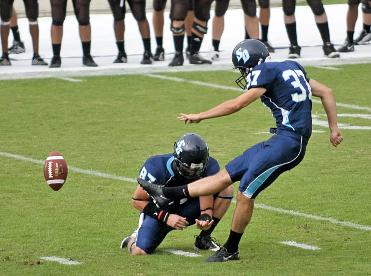 a pair of football players playing a game with their coach in the background