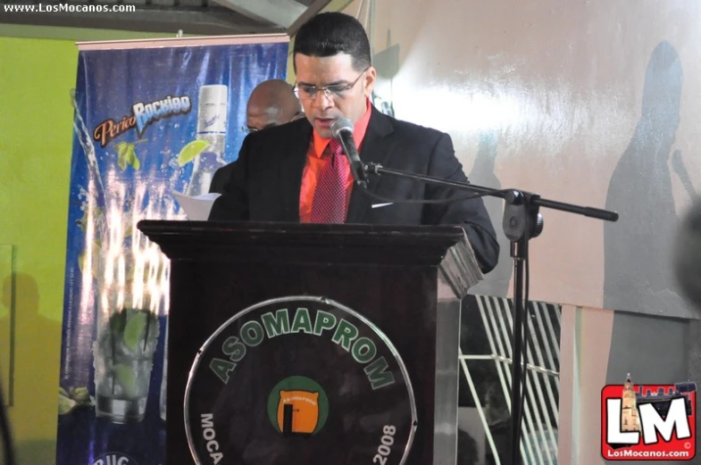 a man wearing a red tie and suit speaks from a podium