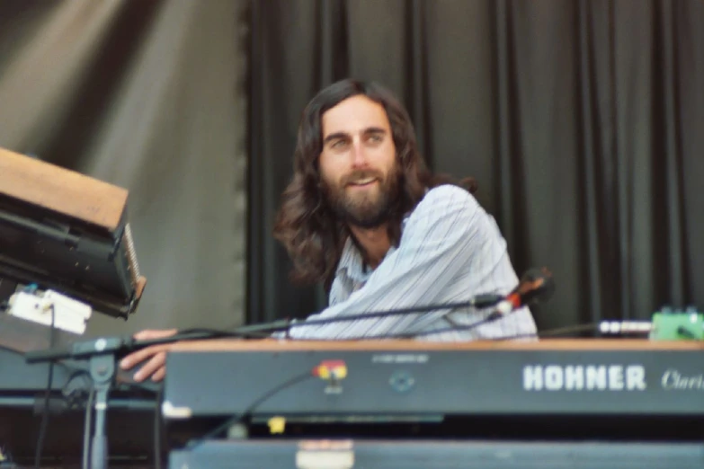 a man with long hair and a beard sitting at a keyboard