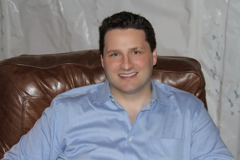 a man sitting on a brown chair smiling