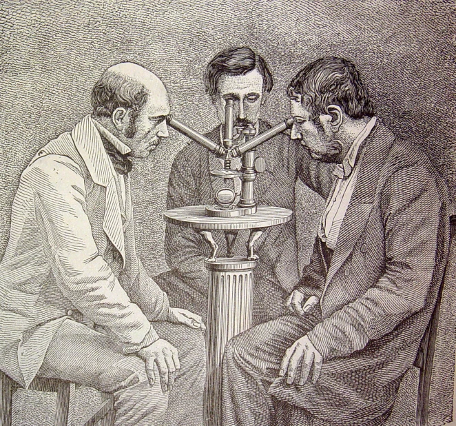 two men working with a small device and another man behind