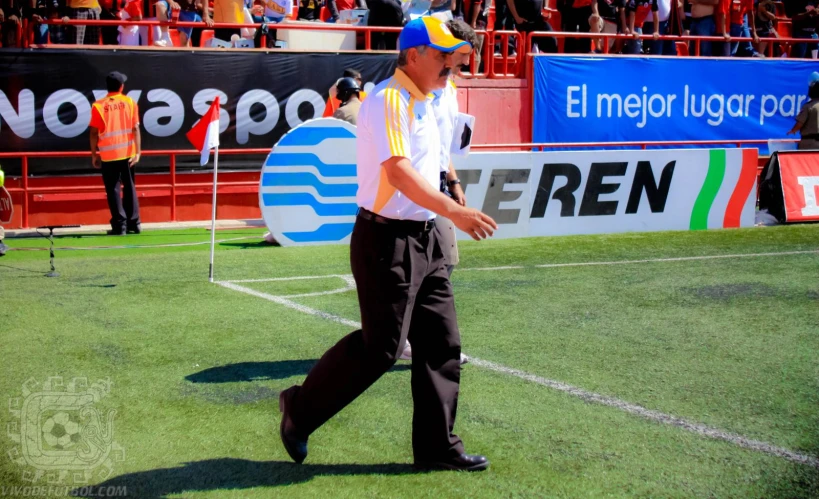 a man wearing a yellow and blue hat walks on the grass