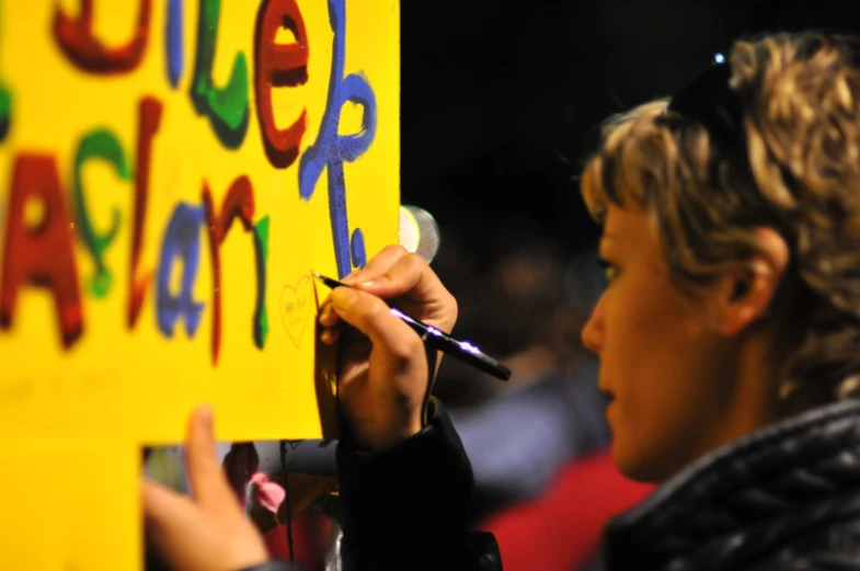 a child's hand holding marker writing on a sign