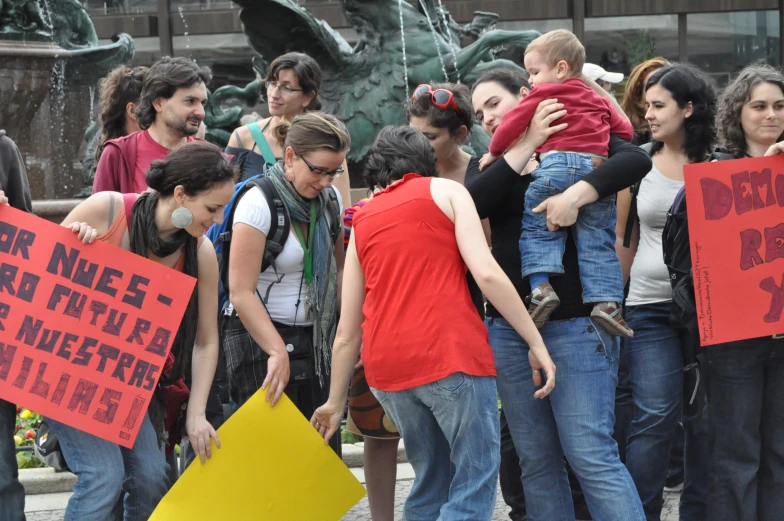 people standing in front of a fountain holding up red signs