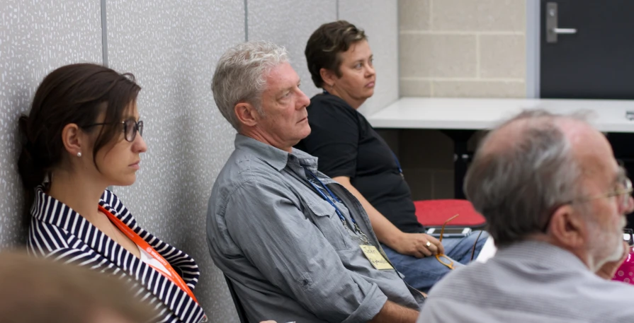 three people sitting in an area talking and others looking on