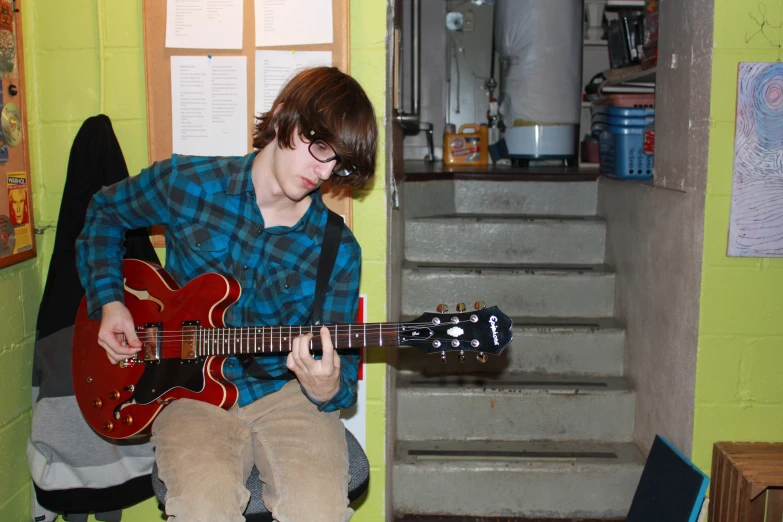 a boy sitting and playing an electric guitar in a house