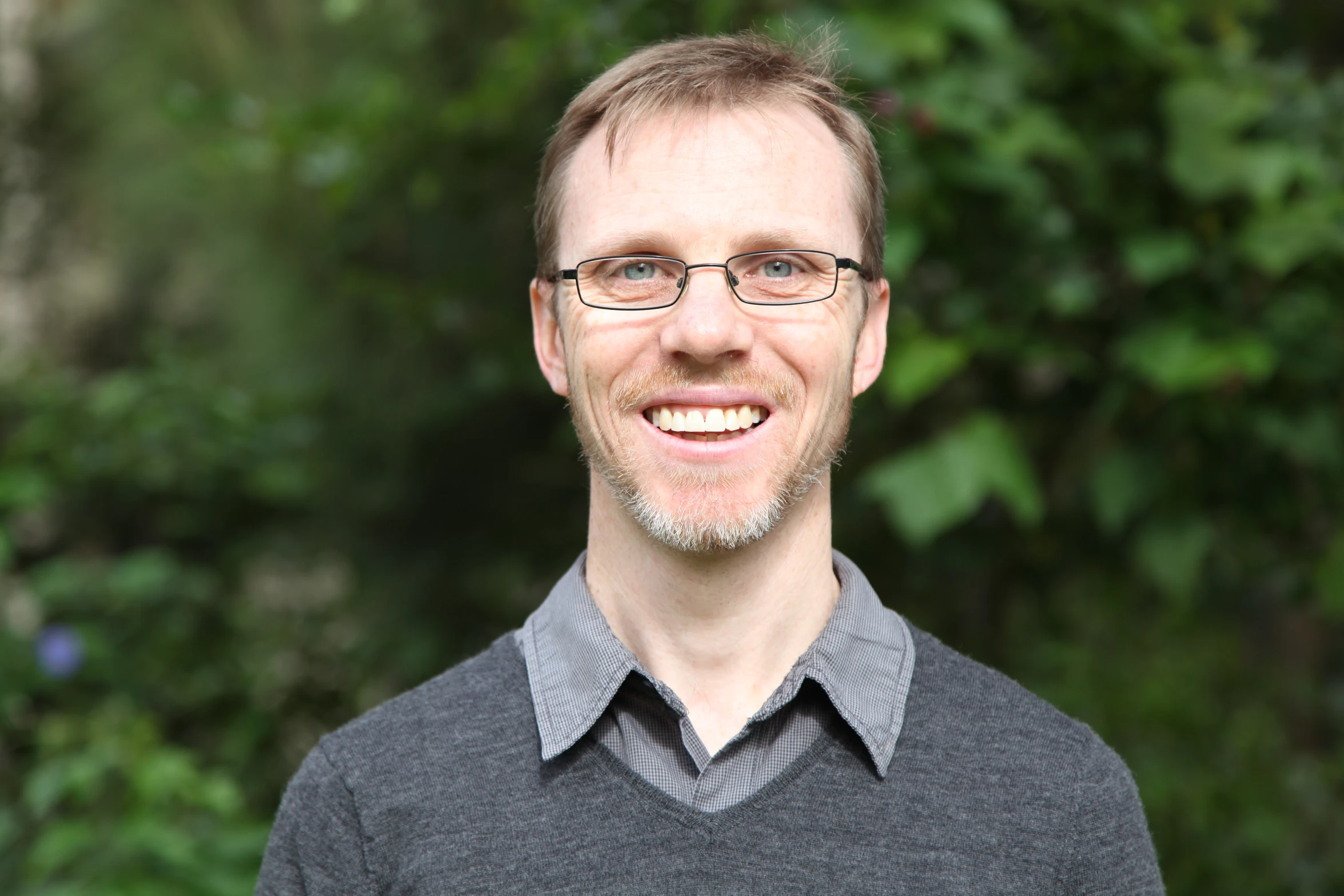 a smiling man with glasses, wearing a black sweater and gray shirt