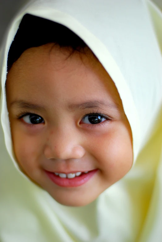 a smiling child with a white blanket on her head