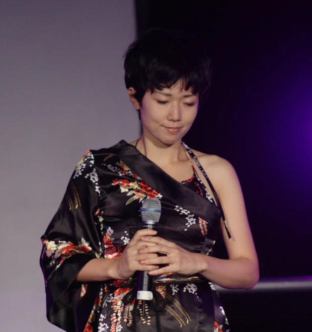 a lady standing and holding a microphone in one hand and wearing a dark print dress
