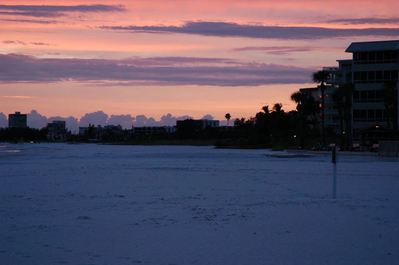 a beach with buildings in the background and pink sunset