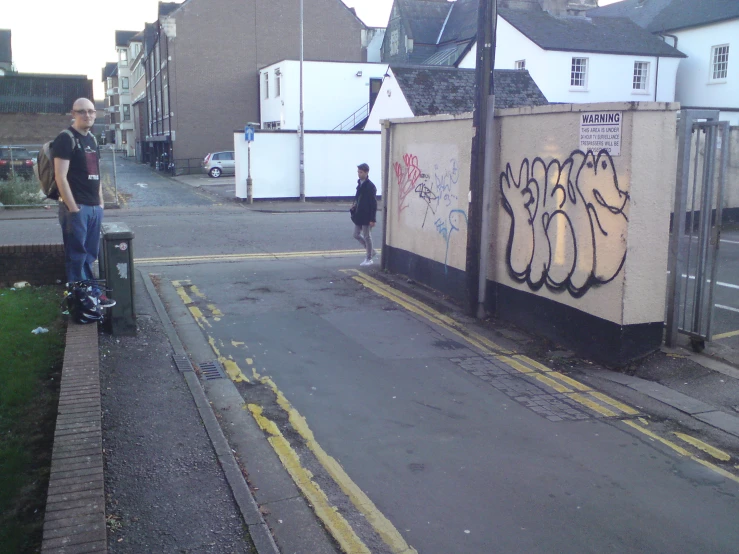 two people are walking on the sidewalk beside a wall with graffiti