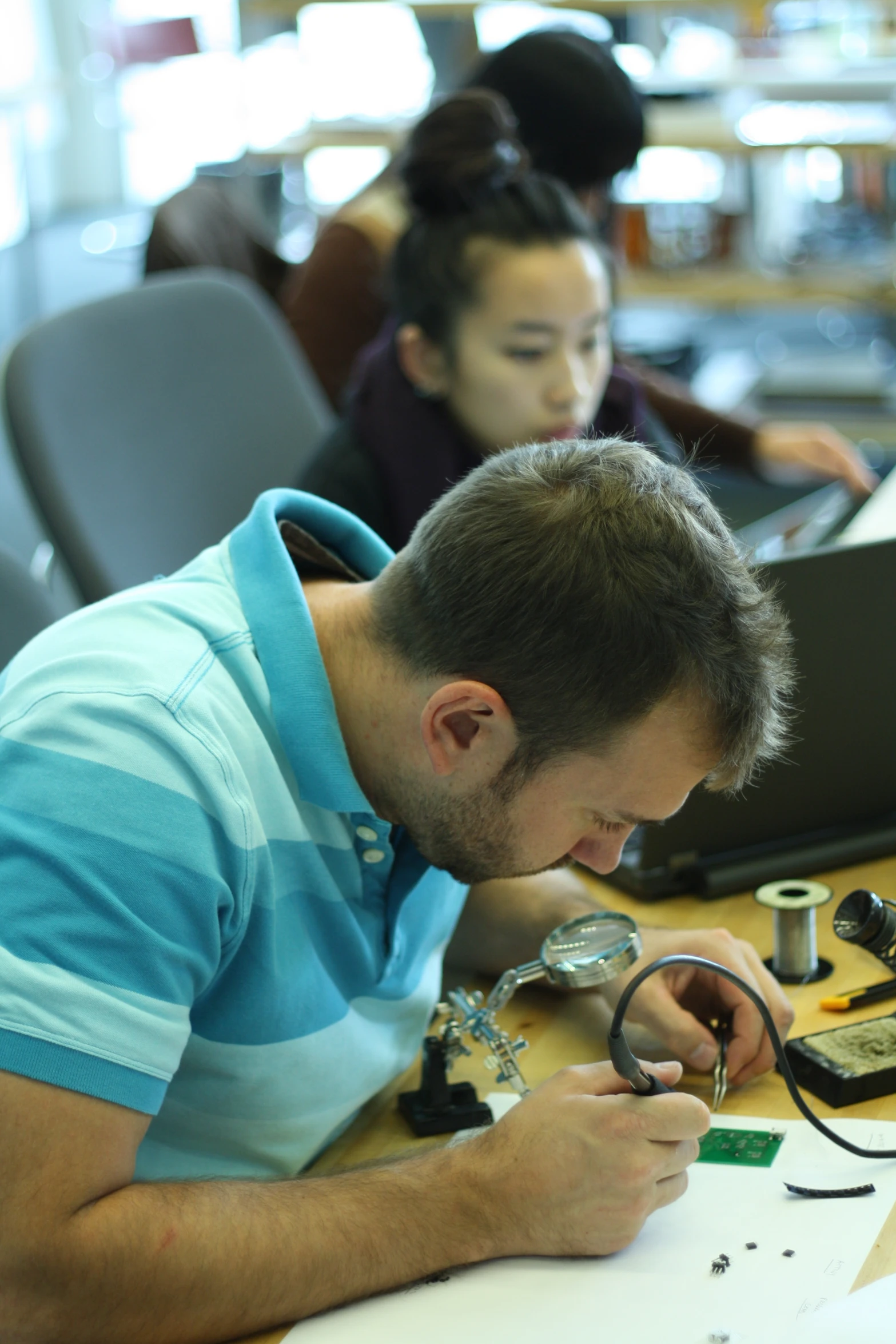 a man working on an electronic project with a woman sitting behind him