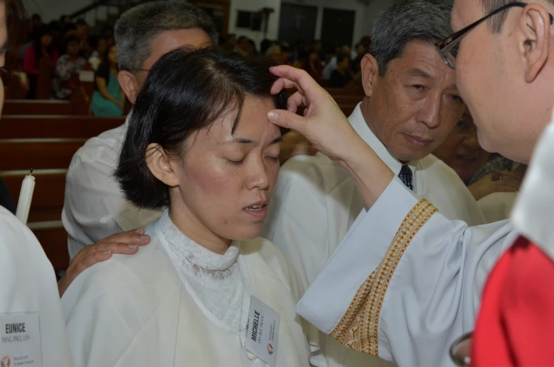 a woman wearing a white dress and a priest are adjusting her hat