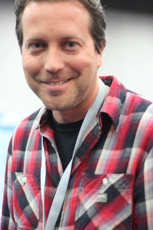 man wearing a red and black plaid shirt smiling at the camera