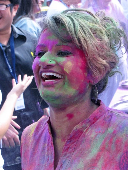 a woman in pink and green painted clothes is smiling